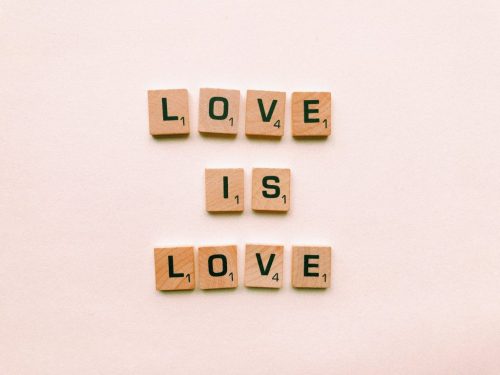 Scrabble tiles spelling out "Love is Love" against a pink background