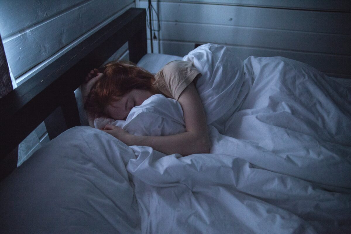 A white woman sleeping curled up in a bed, the colours slightly washed out