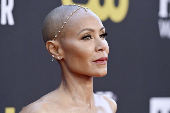 Jada Pinkett Smith on the red carpet- a black woman with a shaved head wearing a jewelled headdress and very long eyelashes