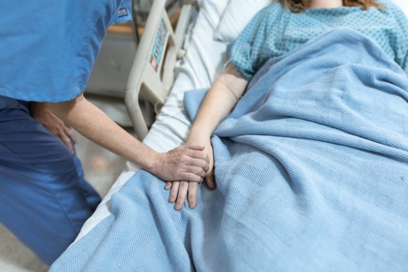a medical professional holding the hand of a patient who is lying in bed